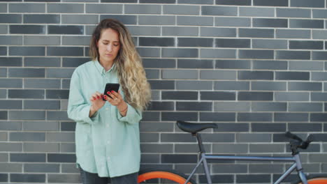Woman-Standing-with-Bike-on-Street-and-Using-Smartphone
